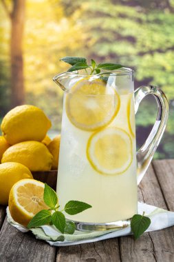 Limon dilimli bir sürahi limonata ve kırsal arka planda eski bir tahta masada nane şekeri.