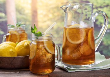 Bir bardak buzlu çay, naneli, limonlu ve buzlu açık hava ahşap masa kırsal yaz arka planlı.