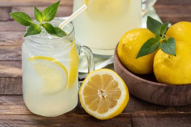 Bir bardak soğuk limonata, nane şekeri, limon dilimleri ve ahşap bir masada buz.