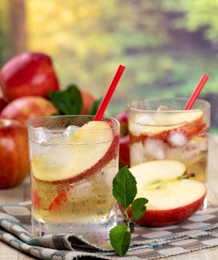 Elma suyunu elma dilimiyle tazelemek ve yaz arkaplanlı bir bardakta buz.