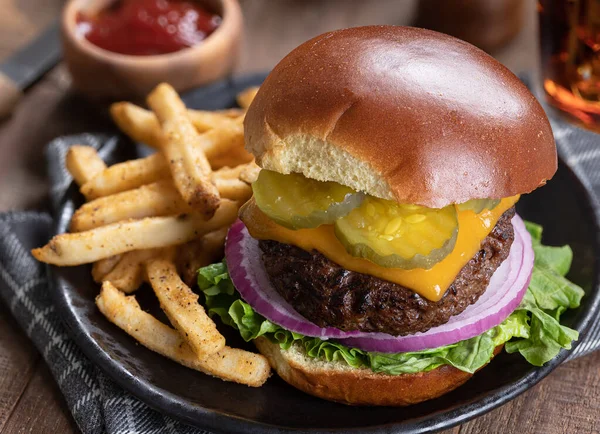 Cheeseburger with pickles, onions and lettuce and french fries on a black plate