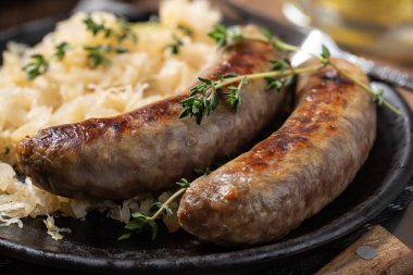 Closeup of bratwurst dinner with sauerkraut garnished with thyme on a black plate