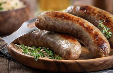Closeup of fried bratwurst garnished with thyme on a plate on a rustic wooden table