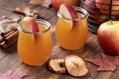 Two glasses of apple cider with fresh apple slices an a rustic wooden table