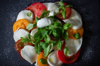 Siyah tabakta taze ev yapımı Caprese salatası. Mozzarella, fesleğen ve üç çeşit domates. İtalyan mutfağı. Aperatif. Üst Manzara. Düz yatıyordu.