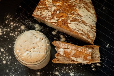 Loaf of artisan wheat and rye bread with graham flour. Sourdough starter on dark background. Top view.