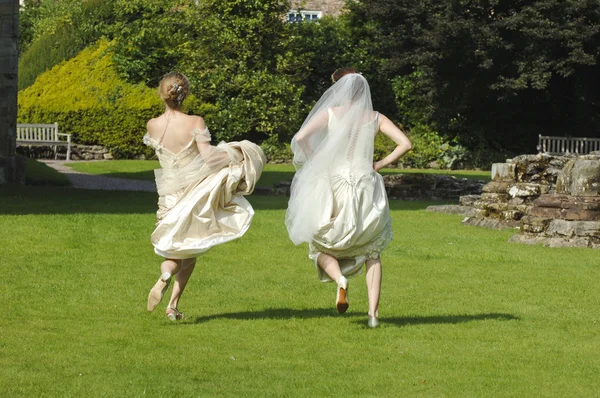 Duas mulheres em vestidos de noiva correndo em um gramado — Fotografia de Stock