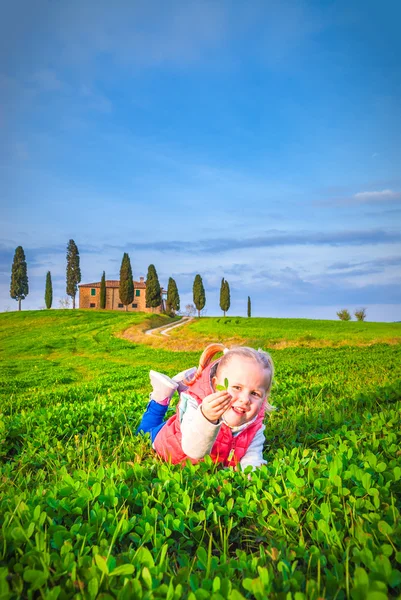 Klein meisje glimlachend en spelen op een weide voor een Toscaanse — Stockfoto