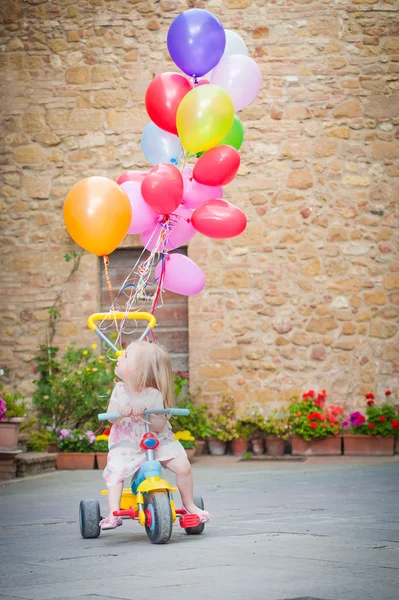 Balonlarla üç tekerlekli bisiklet üzerinde küçük kız — Stok fotoğraf