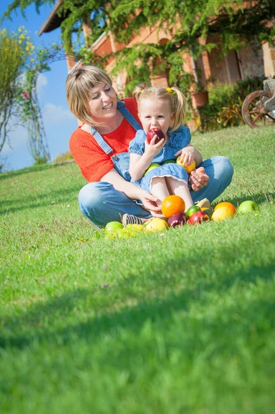 Anya és lánya, enni a színes gyümölcs, zöld fű — Stock Fotó