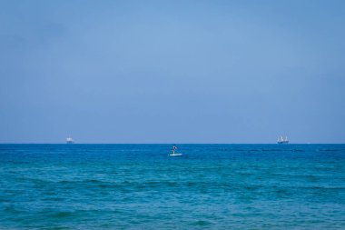 Sakin deniz yüzeyi. Bir kız sörf tahtasında yüzüyor. Ufuktaki gemilerin siluetleri. Arkaplan olarak kullanılabilir.