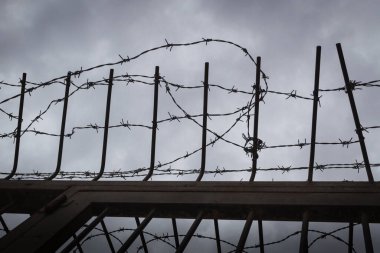 Özgürlüğün kısıtlanmasının sembolü olarak kasvetli bir gökyüzüne karşı dikenli tel..