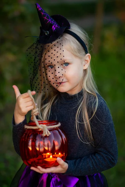 a 5-year-old girl dressed as a witch, a witch\'s hat, a pumpkin-shaped flashlight, street photography, shooting in the fall, preparing for Halloween, emotions of joy and mystery, portrait of a child in a costume for halloween