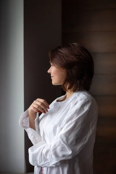Güzel esmer kadın pencerede gömlek ve pijama giyer, fotoğraf pozu verir, poz verir, modellik, mankenlik, depresyon, depresyon, bezginlik, sabah ritüelleri eğitimi alır.