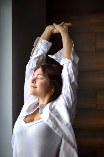 Güzel esmer kadın pencerede gömlek ve pijama giyer, fotoğraf pozu verir, poz verir, modellik, mankenlik, depresyon, depresyon, bezginlik, sabah ritüelleri eğitimi alır.