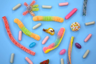 Mavi arka planda farklı şekillerde ve renklerde tatlılar. Jöleli şekerler ve cep manzarası. Çok farklı tatlılar var.. 