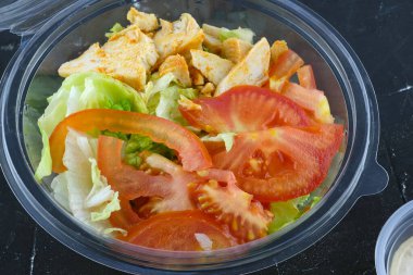 Siyah arka planda domatesli salata, tavuk ve lahana. Tek kullanımlık kasede et ve sebzeli salata. Paket yemek. Öğle yemeği için plastik kap.. 