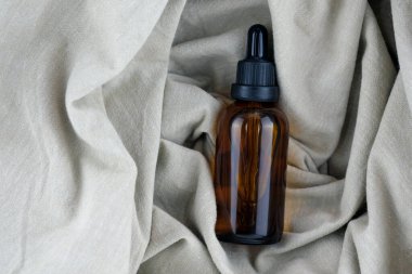 Arka planda keten kumaştan bir pipetle cam şişe, üst manzara. Kahverengi bir yağ şişesi. Cam kozmetik kaplar. Şişede sebze yağı. 