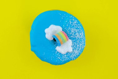 Sarı arka planda gökkuşağı olan parlak bir çörek ve mesaj için yer var. Mavi şekerli çörek, beyaz bulutlar, hindistan cevizi taneleri ve gökkuşağı manzaralı. Delikli tatlı yuvarlak donut.. 