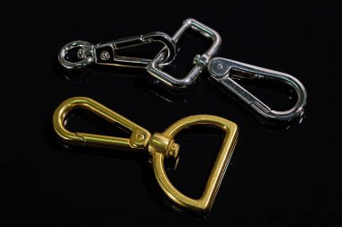 Siyah arka planda metal karabina seti. Çantalar için aksesuarlar. Aksesuar yapmak için kullanılan küçük bir karabina. Çanta aksesuarları. Giyim endüstrisi için metalik ürünler. 