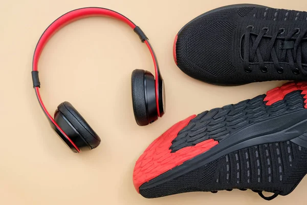 Ακουστικά Κόκκινα Και Μαύρα Sneakers Μπεζ Φόντο Αθλητικές Δραστηριότητες Μουσική — Φωτογραφία Αρχείου