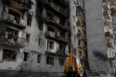 Penceresiz, yanmış, yıkık dökük bir apartman. Ukrayna 'daki bombardıman ve askeri operasyonlar sırasında hasar görmüş. Evin altında, traktör alanı tuzaklardan ve tuğlalardan temizliyor..