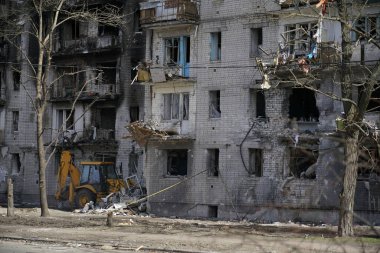 Penceresiz, yanmış, yıkık dökük bir apartman. Ukrayna 'daki bombardıman ve askeri operasyonlar sırasında hasar görmüş. Evin altında, traktör alanı tuzaklardan ve tuğlalardan temizliyor..