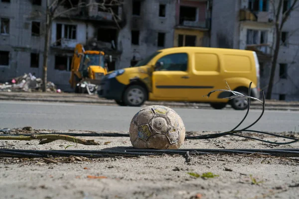 A children\'s soccer ball lies near the road against a building destroyed by an explosion in the war in Ukraine. Nearby are the wires of a broken power line.