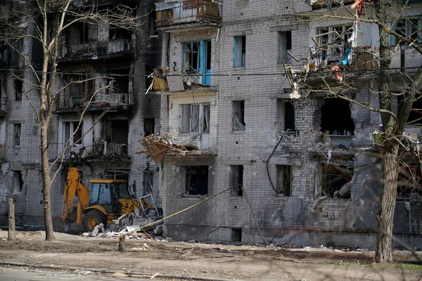 Penceresiz, yanmış, yıkık dökük bir apartman. Ukrayna 'daki bombardıman ve askeri operasyonlar sırasında hasar görmüş. Evin altında, traktör alanı tuzaklardan ve tuğlalardan temizliyor..