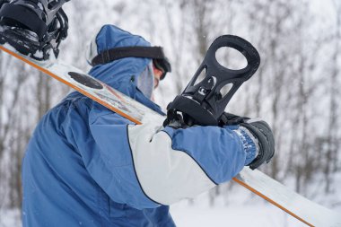 Freerider kar tozunun içinden geçiyor. Elinde bir snowboard tutuyor.