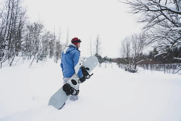 Freerider kar tozunun içinden geçiyor. Elinde bir snowboard tutuyor.