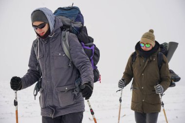 Kış kıyafetli iki adam karda yürüyorlar. Kontrol kutbuna kış seferi. Bir adam büyük bir sırt çantası taşıyor.