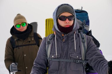 Gözlüklü, şapkalı ve kışlıklı iki adam karda yürüyorlar. Kutup bölgesine kış gezisi