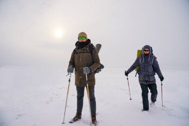 Kış kıyafetli iki adam karda yürüyorlar. Kontrol kutbuna kış seferi. Bir adam büyük bir sırt çantası taşıyor.