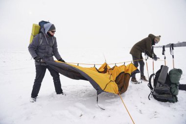İki adam karda bir çadır kuruyor. Kış seferi sırasında aşırı koşullarda bir çadır kurmak. Kış yürüyüşü