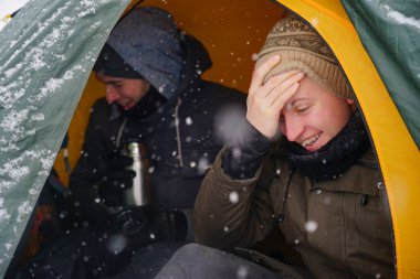 Çocuklar bir çadırda oturuyor, kış yürüyüşü sırasında yemek hazırlıyorlar. Karda çadırın yanında ekipmanları yatıyor. İki adam çadırda yemek yiyor. Keşif sırasında kışın turistlere yemek servisi.