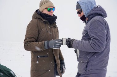 Çocuklar termo bardaklardan sıcak çay içip termostan su döküyorlar. Kış seferi boyunca çadırın yanında dururlar..