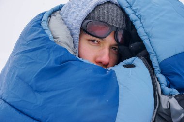 Portrait of a guy in a sleeping bag during the winter expedition.	