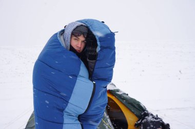 Portrait of a guy in a sleeping bag during the winter expedition.	