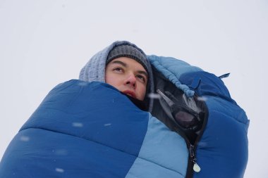 Portrait of a guy in a sleeping bag during the winter expedition.	