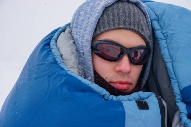 Portrait of a guy in a sleeping bag during the winter expedition.	