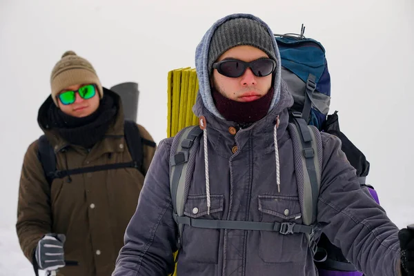Gözlüklü, şapkalı ve kışlıklı iki adam karda yürüyorlar. Kutup bölgesine kış gezisi