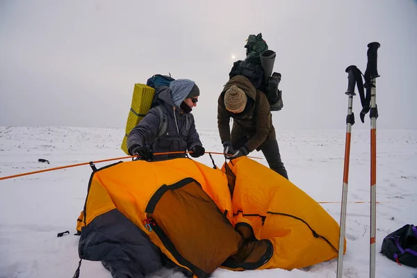 İki adam karda bir çadır kuruyor. Kış seferi sırasında aşırı koşullarda bir çadır kurmak. Kış yürüyüşü