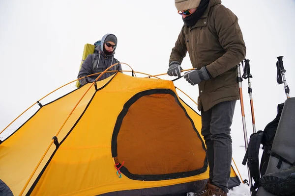 İki adam karda bir çadır kuruyor. Kış seferi sırasında aşırı koşullarda bir çadır kurmak. Kış yürüyüşü