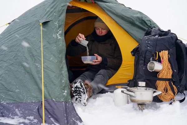 Çocuklar bir çadırda oturuyor, kış yürüyüşü sırasında yemek hazırlıyorlar. Karda çadırın yanında ekipmanları yatıyor. İki adam çadırda yemek yiyor. Keşif sırasında kışın turistlere yemek servisi.
