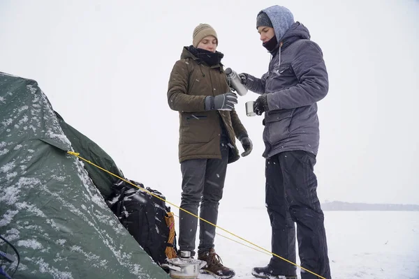 Çocuklar termo bardaklardan sıcak çay içip termostan su döküyorlar. Kış seferi boyunca çadırın yanında dururlar..