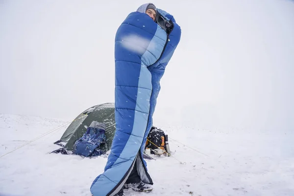 man in a sleeping bag in winter near the tent