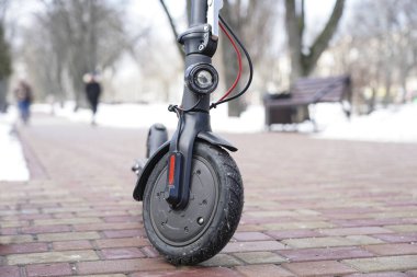 Parkta yakın planda elektrikli scooter var. Dışarısı soğuk ve karlı. İlkbaharda kar altında scooter.