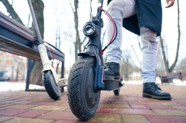 Parkta yakın planda elektrikli scooter var. Dışarısı soğuk ve karlı. İlkbaharda kar altında scooter.