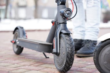 Parkta yakın planda elektrikli scooter var. Dışarısı soğuk ve karlı. İlkbaharda kar altında scooter.